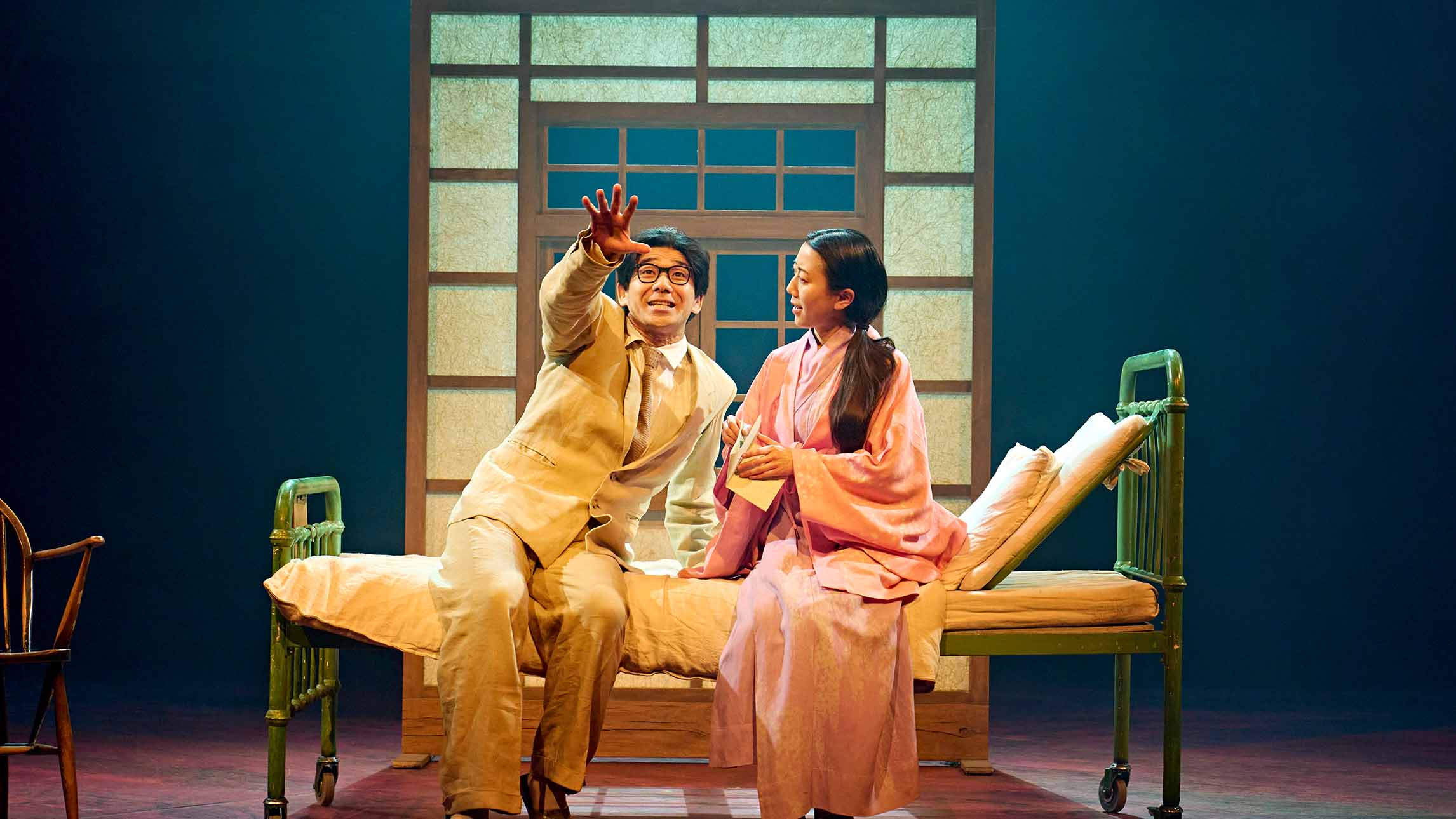 Two actors sitting on a bed from My Neighbour Totoro theatre production at the Gillian Lynne Theatre, London