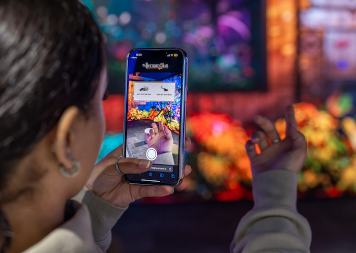 A woman captures a digital butterfly on her finger at The Butterfly Trail at Outernet